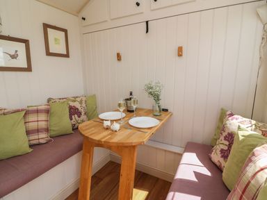 A small dining nook with wooden table set with two plates glasses and decorations at Shepherd's View in Rhayader