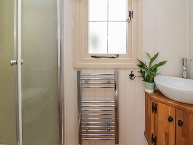A bathroom with a shower cabin a chrome towel rail a window and a wooden vanity unit with a plant and a white sink at Shepherd's View in Rhayader