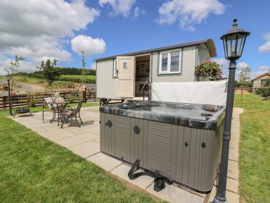An outdoor area with a hot tub table and chairs near a small cabin and lamp posts at Shepherd's View in Rhayader