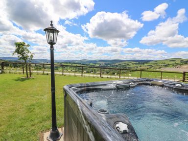 An outdoor hot tub next to a lamp post with a grassy yard and hills in the background at Shepherd's View in Rhayader