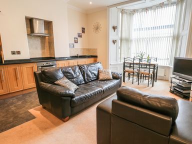 An open plan living room and kitchen with a black leather sofa and armchair a dining table with four chairs and a television at Flat 4 in Whitby