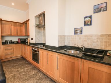 A kitchen with wooden cabinets black countertops oven stove microwave and sink at Flat 4 in Whitby