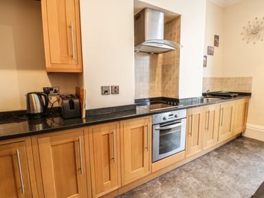 A kitchen with wooden cabinets black countertop stainless steel oven kettle and toaster at Flat 4 Whitby