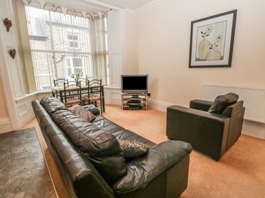A living room with black leather sofa armchair dining table and television at Flat 4 in Whitby