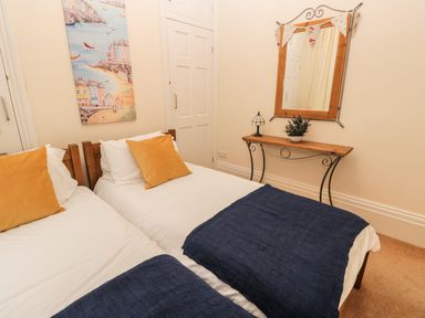 A bedroom with two single beds a wooden console table with a mirror and artwork on the wall at Flat 4 Whitby