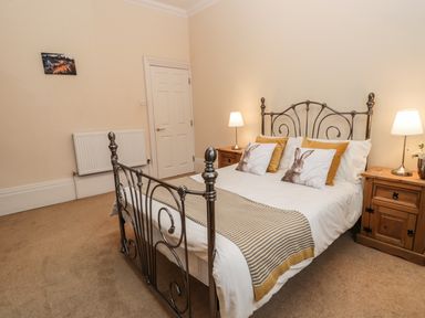 A bedroom with a metal bed frame bedside tables with lamps and cushions with rabbit prints at Flat 4 in Whitby
