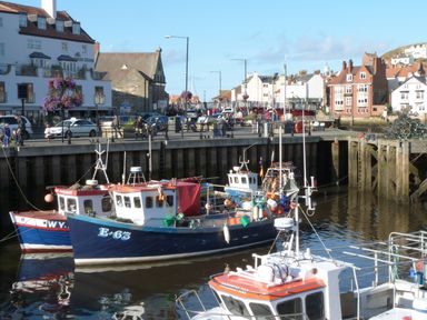 Fishing boats docked in a harbor with people walking along the quay and buildings in the background at Flat 4 in Whitby