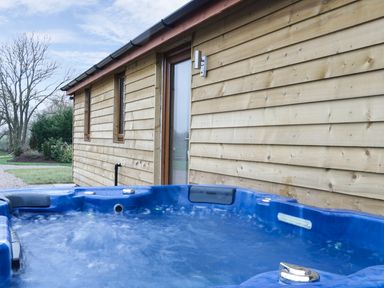 An outdoor hot tub next to a wooden building with glass door and small windows at Gardener's Lodge in Nantwich