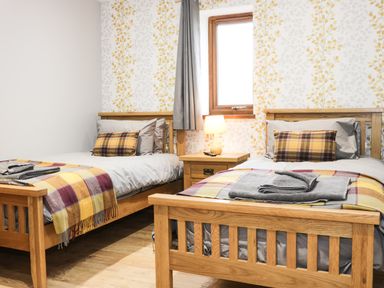 A bedroom with two wooden single beds with plaid cushions and blankets a wooden nightstand with a lamp and a window at Gardeners Lodge in Nantwich