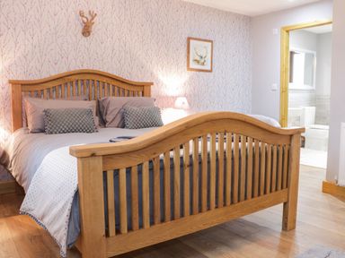 A bedroom with a wooden bed frame a bedside lamp and an open door leading to a bathroom at Gardener's Lodge in Nantwich
