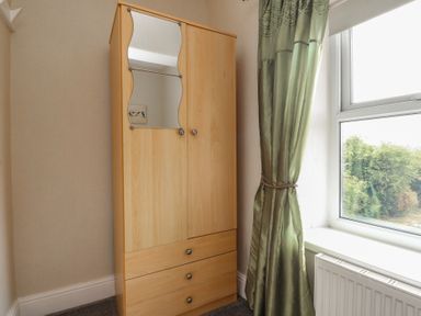 A wardrobe and window with curtain in a bedroom at The Farmhouse in Brynsiencyn near Newborough