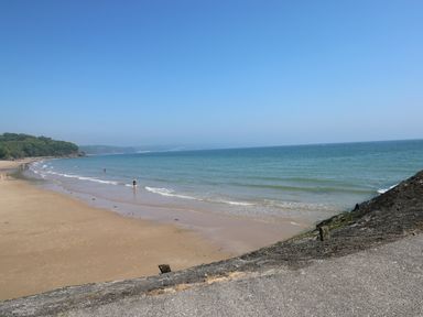 A sandy beach with people near the water and a forested area on the left at Sandy Bay House in Saundersfoot