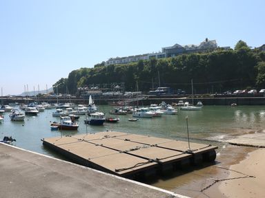 Boats moored in a harbor with a floating dock and buildings on a hill at Sandy Bay House in Saundersfoot
