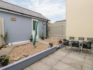 An outdoor patio area with a gravel garden and a covered umbrella next to a dining table with chairs at Sandy Bay House in Saundersfoot