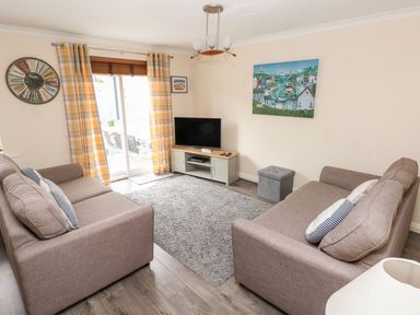 A living room with two sofas a television on a stand and a large wall clock at Sandy Bay House in Saundersfoot