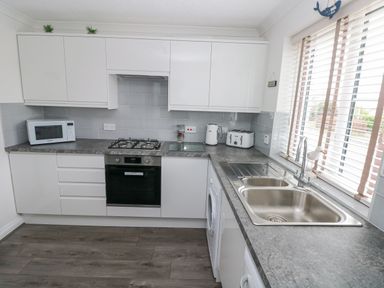 A kitchen with white cabinets microwave oven kettle toaster and stainless steel sink at Sandy Bay House in Saundersfoot
