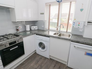 A kitchen with a gas stove oven washing machine double sink toaster kettle and dishwasher with window blinds at Sandy Bay House in Saundersfoot