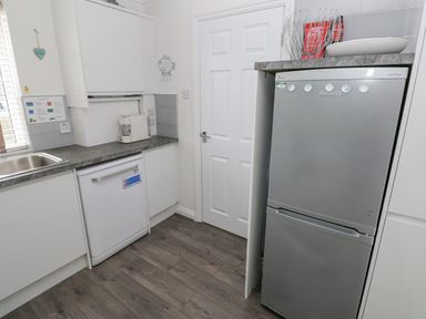 A kitchen with a dishwasher a refrigerator a coffee machine and a door at Sandy Bay House in Saundersfoot