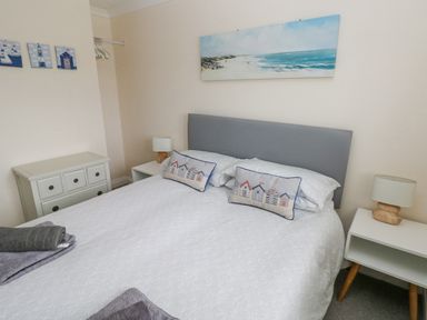 A bedroom with a double bed with pillows and white bedding bedside tables with lamps a dresser and wall art at Sandy Bay House Saundersfoot
