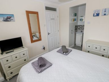 A bedroom with a bed covered in white bedding and towels on top a TV on a dresser a wall mirror and a doorway leading to a small bathroom at Sandy Bay House in Saundersfoot
