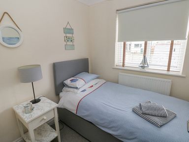 A bedroom with a single bed a nightstand with a lamp and a window with blinds at Sandy Bay House in Saundersfoot