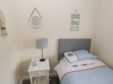 A bedroom corner with a single bed a bedside table with a lamp and a round mirror on the wall at Sandy Bay House in Saundersfoot