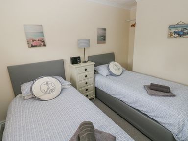 A bedroom with two single beds a nightstand with a lamp and radio and nautical decor at Sandy Bay House in Saundersfoot