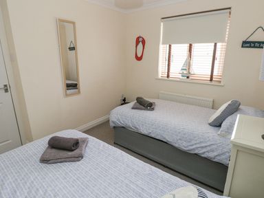 A bedroom with two single beds each with folded towels on top a window with blinds and a model boat on the sill a wall mirror and decorative signs at Sandy Bay House in Saundersfoot