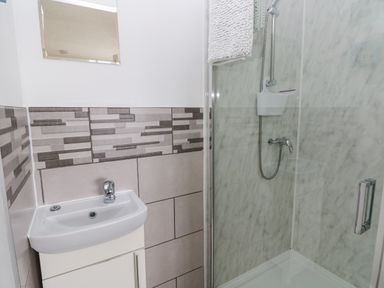 A bathroom with a small white sink and a shower with a glass door at Sandy Bay House in Saundersfoot