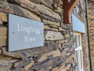 A stone wall with a sign reading Loughrigg View and a window at Loughrigg View in Ambleside