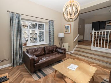 A living room with a brown leather sofa a wooden coffee table and a window with striped curtains at Loughrigg View in Ambleside
