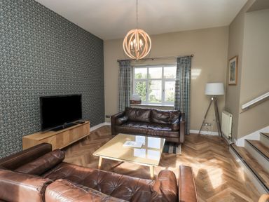 A living room with brown leather sofas a glass coffee table a wooden TV stand with a television and patterned wallpaper at Loughrigg View in Ambleside