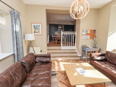 A sitting room with two brown leather sofas a glass coffee table a reading lamp and blue striped curtains at Loughrigg View in Ambleside
