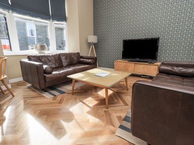A living room with brown leather sofas a wooden coffee table and a television on a wooden stand at Loughrigg View in Ambleside