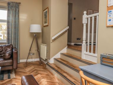 A corner of a room with a brown leather sofa floor lamp stairs a blue desk and a window with striped curtains at Loughrigg View Ambleside