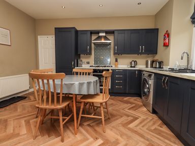 A kitchen with wooden chairs around a round table and dark cabinets with appliances at Loughrigg View in Ambleside