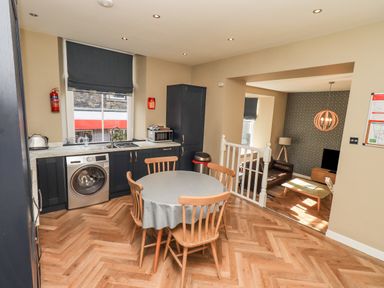 A kitchen with a round table and four wooden chairs a washing machine and microwave next to a window leading to a living room at Loughrigg View in Ambleside