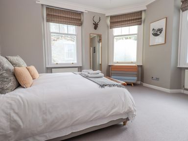 A bedroom with a bed pillows and towels a mirror two windows and a chest of drawers at Loughrigg View in Ambleside