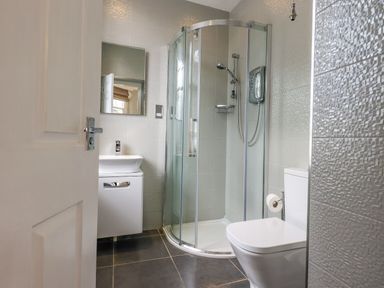 A bathroom with a corner shower unit a toilet and a sink with a mirror above at Loughrigg View Ambleside