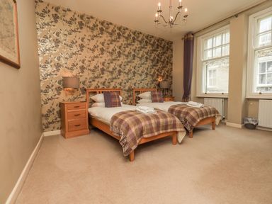 A bedroom with two single beds bedside tables lamps and windows at Loughrigg View in Ambleside
