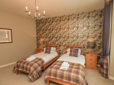 A bedroom with two single beds wooden headboards nightstands with lamps and plaid blankets at Loughrigg View in Ambleside