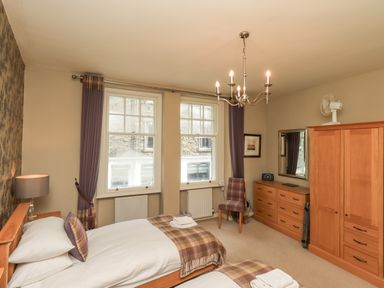 A bedroom with two single beds a wooden wardrobe and dresser with a mirror and a chair at Loughrigg View in Ambleside