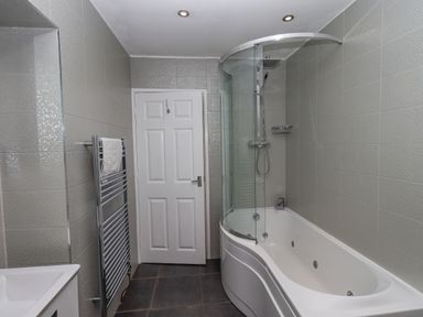 A bathroom with a bathtub and shower door a towel rack and a closed door at Loughrigg View in Ambleside