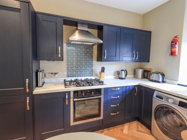 A kitchen with dark cabinets a gas stove oven range hood kettle toaster washing machine and a fire extinguisher on the wall at Loughrigg View in Ambleside