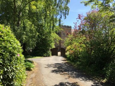 A driveway leading to open gates with trees and shrubs on both sides at Geltsdale East Wing in Wetheral