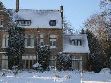 A snow covered stone house with ivy on the walls and trees in the background at Geltsdale East Wing in Wetheral
