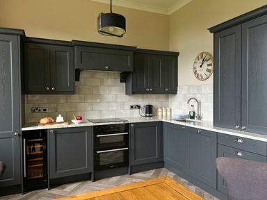 A kitchen with dark cabinets a double oven an electric stove a sink a wall clock and kitchen items on the counter at Geltsdale East Wing in Wetheral