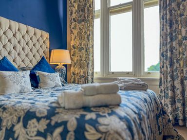 A bedroom with a bed covered in blue and white floral bedding with rolled towels near a window at Geltsdale East Wing in Wetheral