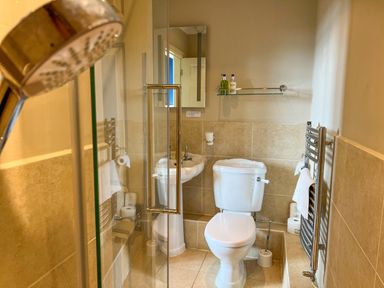 A bathroom with a toilet sink mirror glass shelf showerhead and towel rack at Geltsdale East Wing in Wetheral
