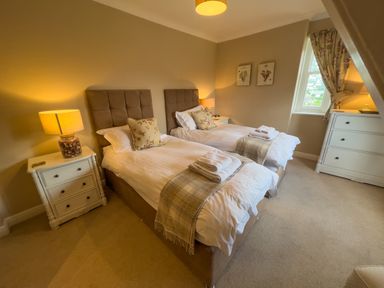 A bedroom with two single beds bedside tables lamps and a dresser at Geltsdale East Wing in Wetheral